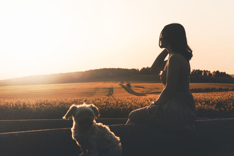 Side view of woman sitting with dog during sunset