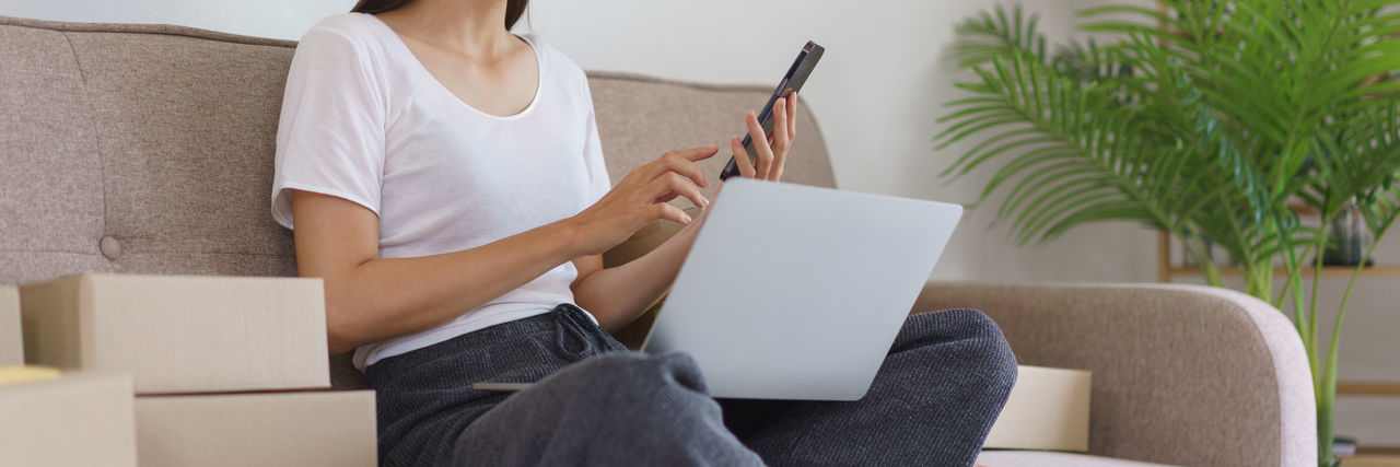 Midsection of woman using digital tablet while sitting on sofa at home