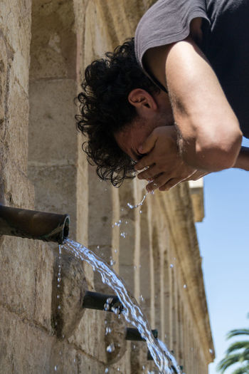 Low angle view of man washing face at drinking fountain