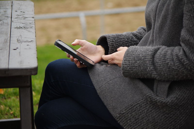 Midsection of woman wearing warm clothing using mobile phone outdoors