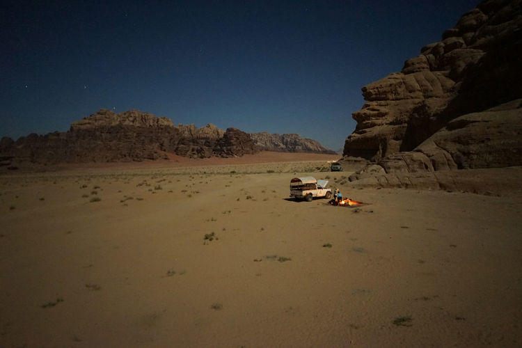 Barren landscape with vehicle and fire by rocky cliff against clear sky