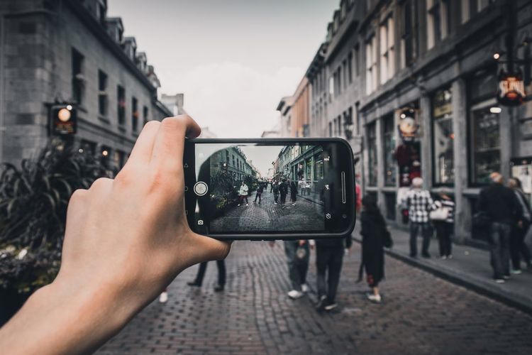 Close-up of man photographing woman using smart phone on street