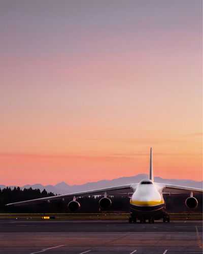 Airplane on runway against sky during sunset