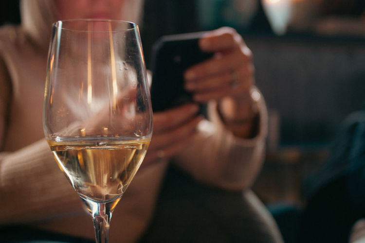 Close-up of wineglass with woman on mobile phone.