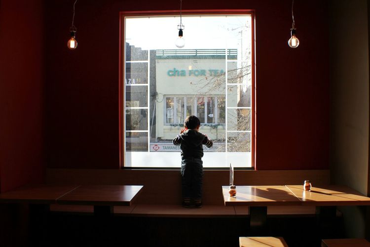 Full length rear view of kid standing by window in restaurant