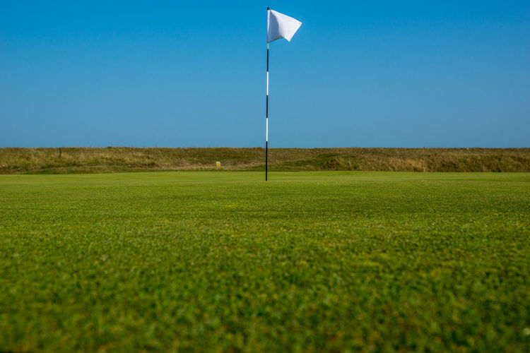 Golf flag on grassy field against clear blue sky