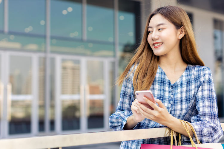Smiling young woman using smart phone while standing outdoors