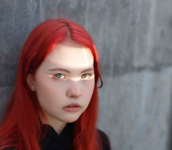 Portrait of a young girl with piercings and red hair, with a ray of sun in her eyes