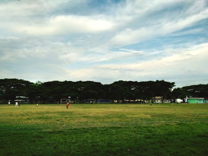 People playing soccer field against sky