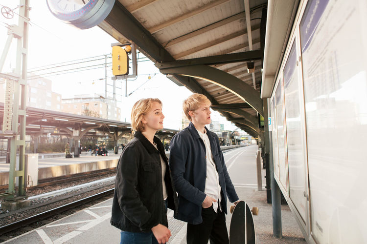 Young couple looking at information board while standing on railroad station platform