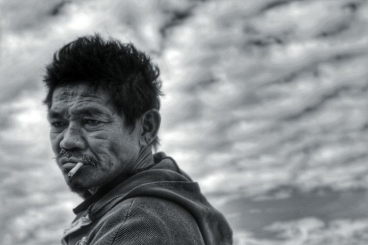 Side view of mature man smoking while standing against cloudy sky