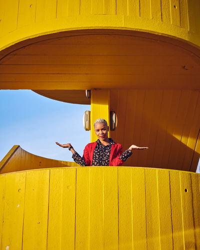Low angle portrait of woman standing at yellow balcony