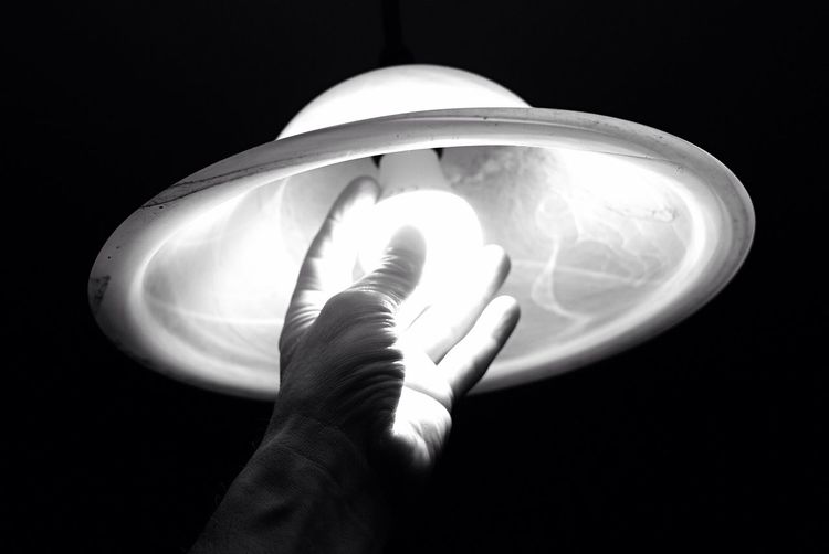 Cropped image of person touching pendant light against black background