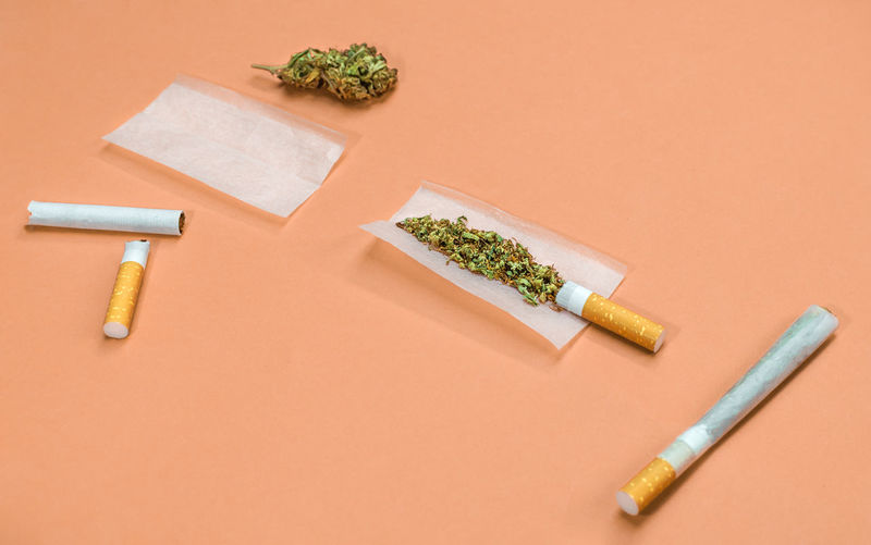 Steps and materials to roll a marijuana joint on orange background.