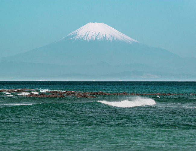 Scenic view of ocean and mt. fuji against misty sky on hot summer morning.
