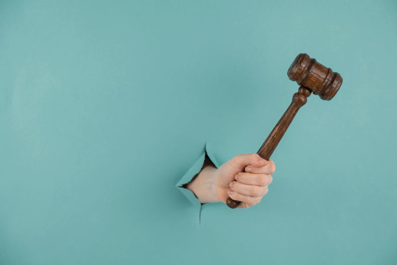 Woman's hand holding a wooden judge's gavel on a blue background