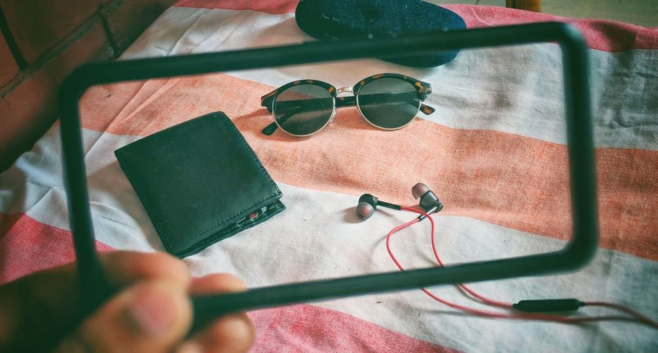 Cropped hand holding frame against purse with sunglasses and in-ear headphones on table