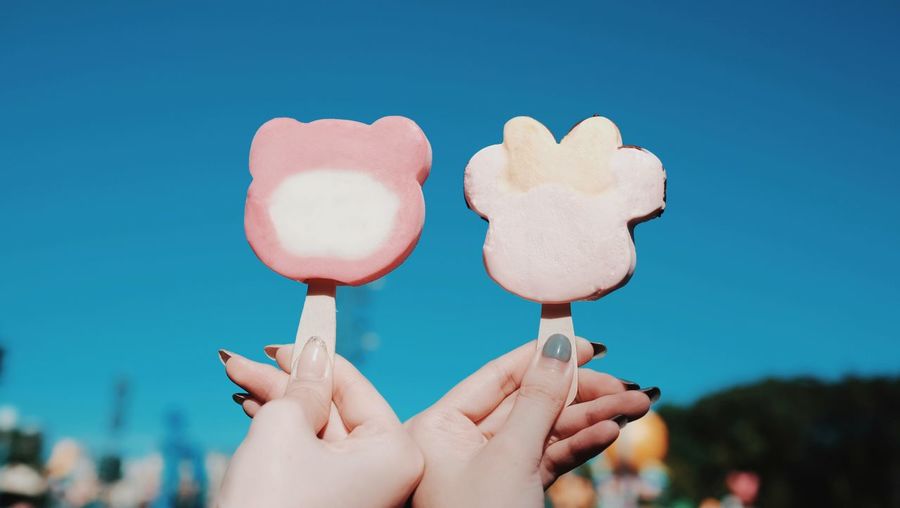 Cropped hand of female friends holding popsicles against clear blue sky