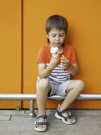 Little boy eats ice cream outdoors. kid on monochrome, bright orange wall background. summer.