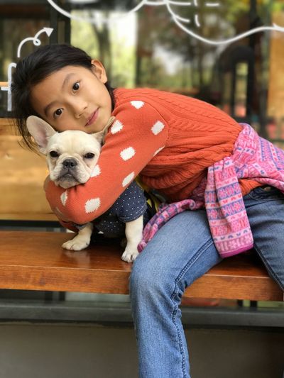 Portrait of cute girl embracing dog while sitting on bench