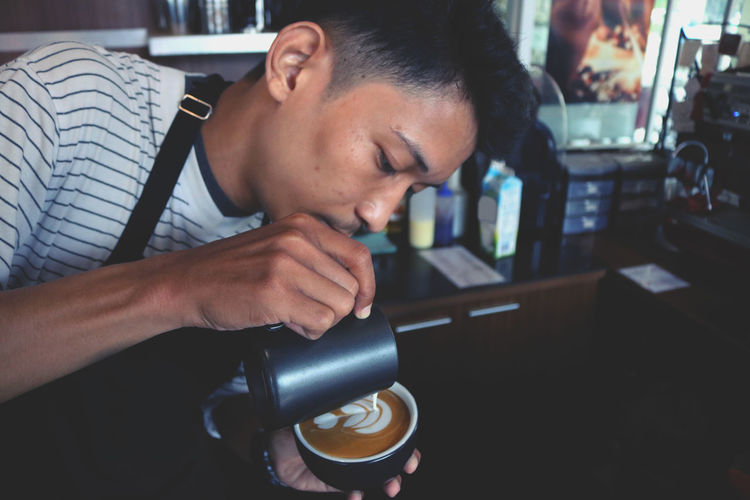 Man pouring milk in coffee at cafe