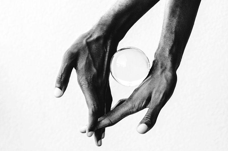 Cropped image of hands balancing crystal ball against white background