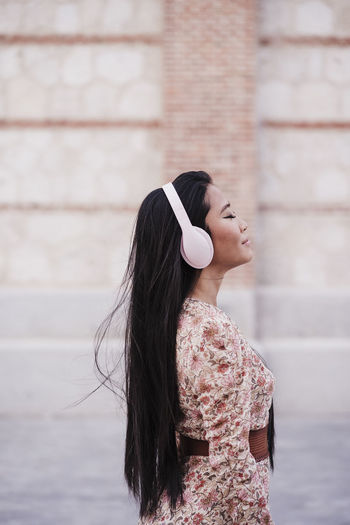 Woman with long hair wearing headphones while standing near wall