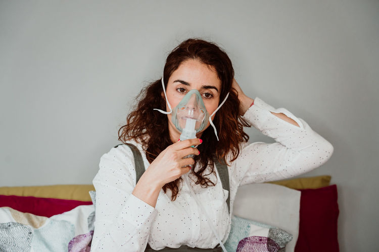 Woman wearing oxygen mask while sitting against wall in hospital