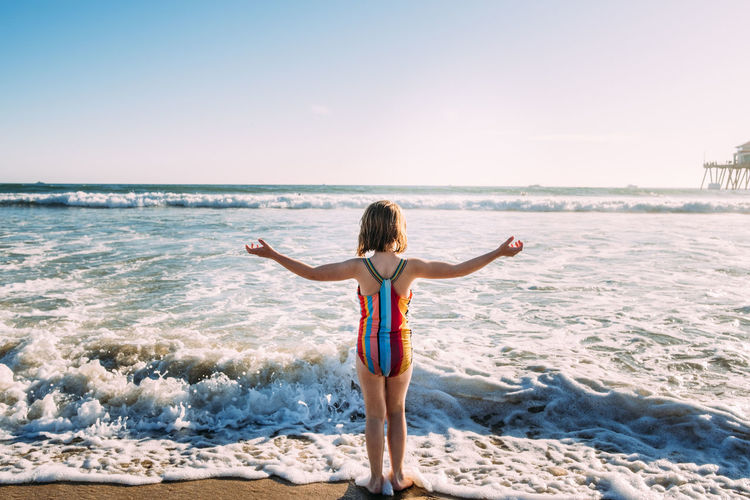Young girl standing at waters edge on beach, facing ocean