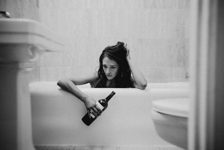 Woman drinking bottle of red win in bathtub alone. rough time. 