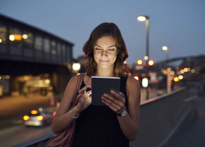 Portrait of smiling woman holding smart phone in city at night