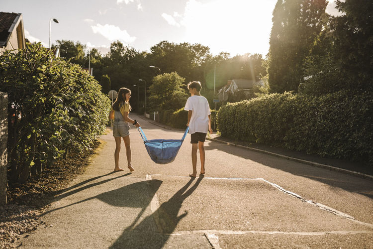 Brother and sister carrying bag on road during sunny day