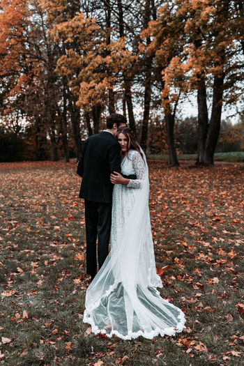 Bride embracing groom while standing on land during autumn