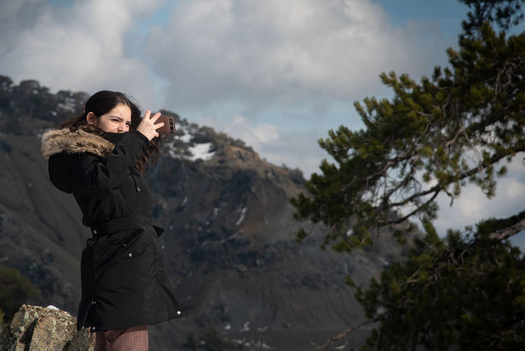 Young attractive teenage girl taking selfie with a mobile phone on a snowy mountain. 