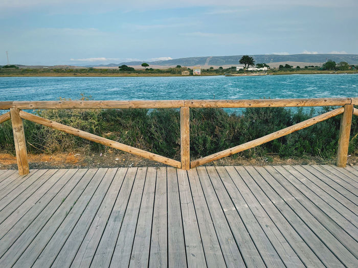 Wooden railing by sea against sky