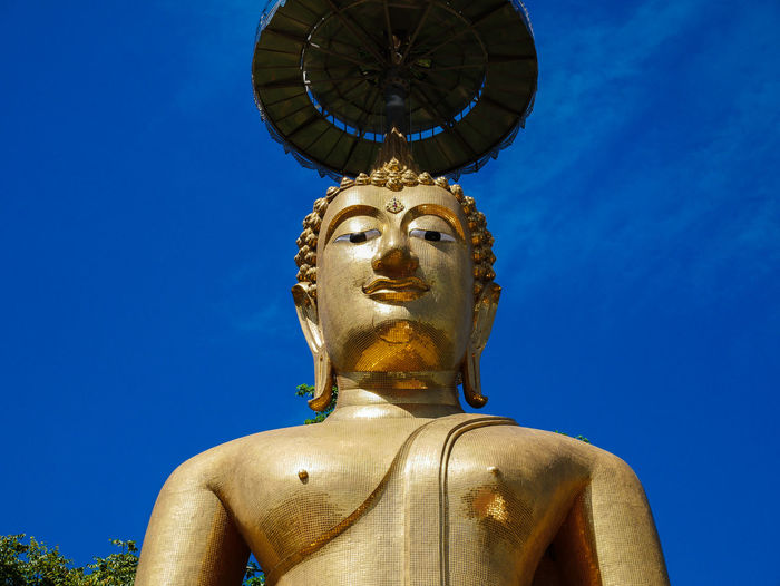 Low angle view of golden buddha statue against blue sky
