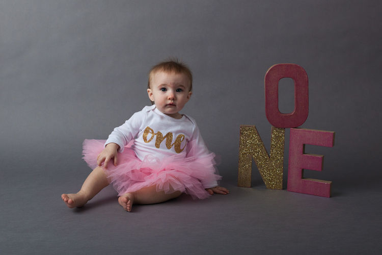 Baby girl sitting with sparkling text over gray background