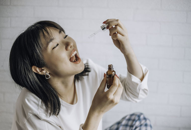 Asian woman dripping cbd oil into mouth for sleep. medical cannabis. vitamins and supplements