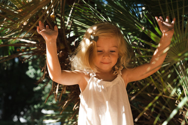 Cute caucasian pretty blonde two year old girl, toddler, kid among big green exotic plants