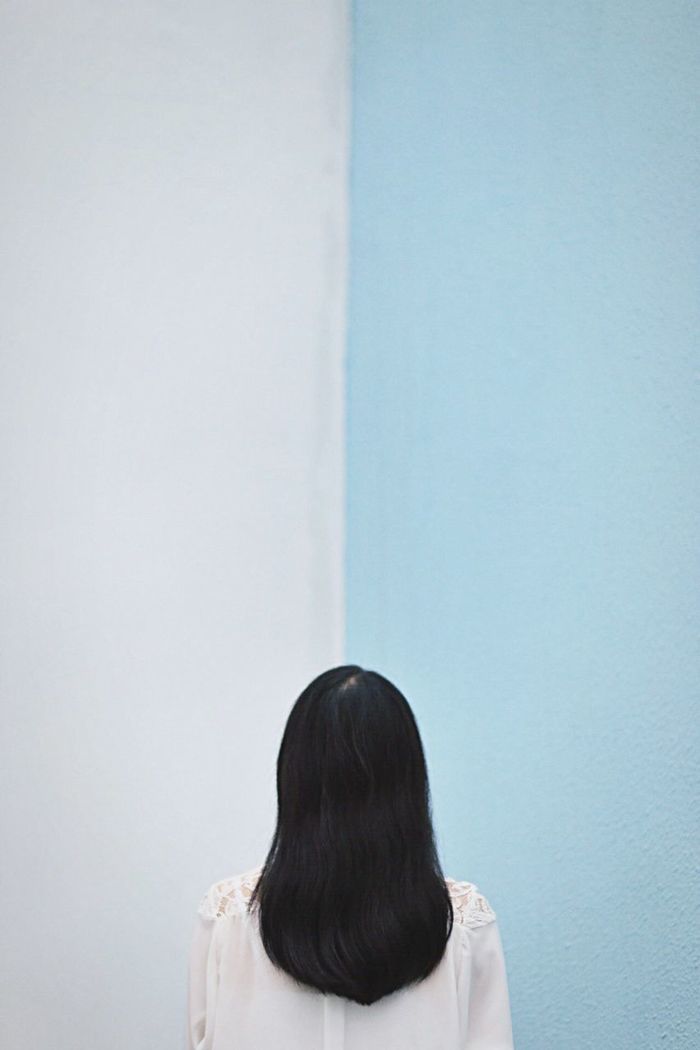 Rear view of woman standing against blue and white wall