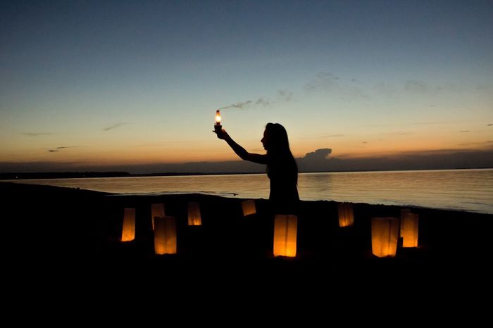 Silhouette woman holding illuminated electric lamp on beach at dusk