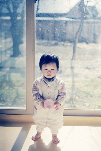 Full length of cute baby girl holding ball while standing against window at home