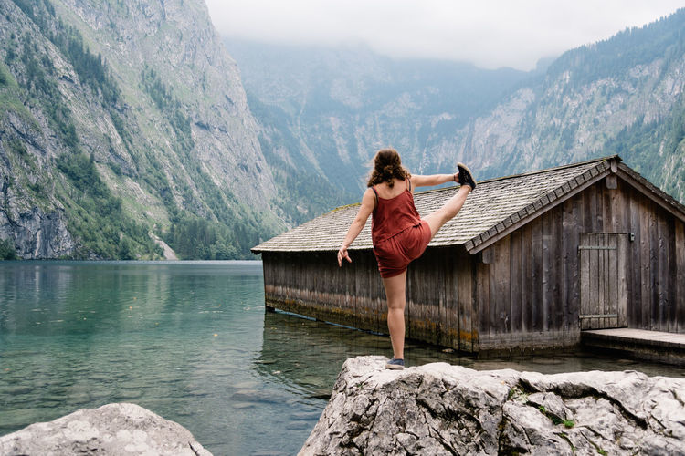 Woman exercising on rock by lake against mountain range