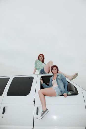 Low angle view of friends sitting on van against clear sky