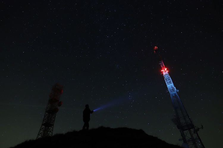 Low angle view of man flashlight on electricity pylon at night