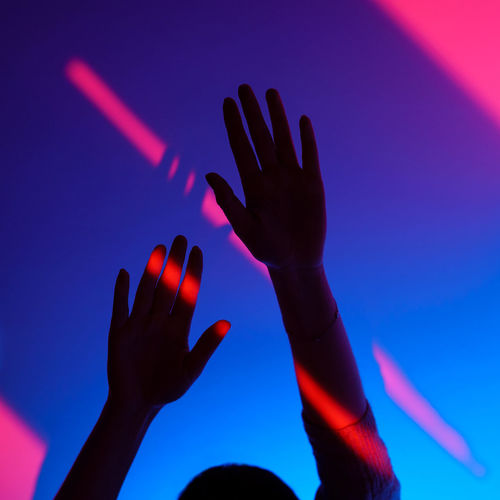 Woman arm gesturing with open hand over fashion blue and pink wall, neon red light on wrist.