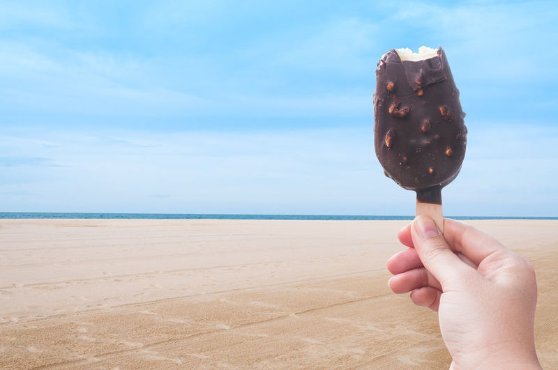 Close-up of hand holding ice cream at beach against sky