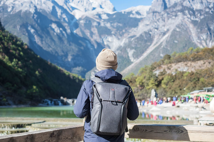 Rear view of man wearing backpack while standing against mountains during winter