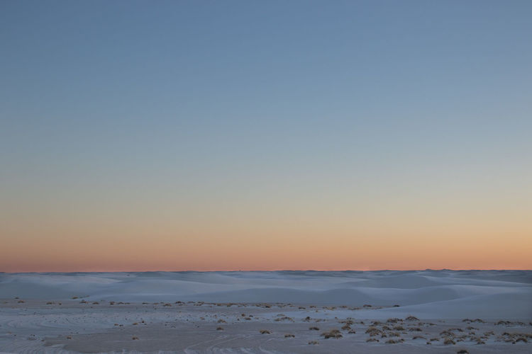 Scenic view of snow covered land against clear sky during sunset