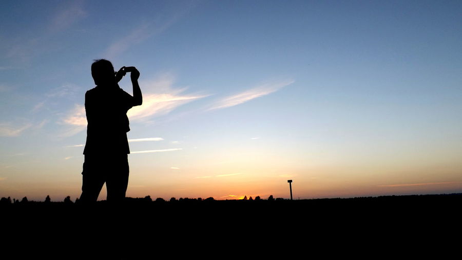 Silhouette of man taking pictures of sunset 